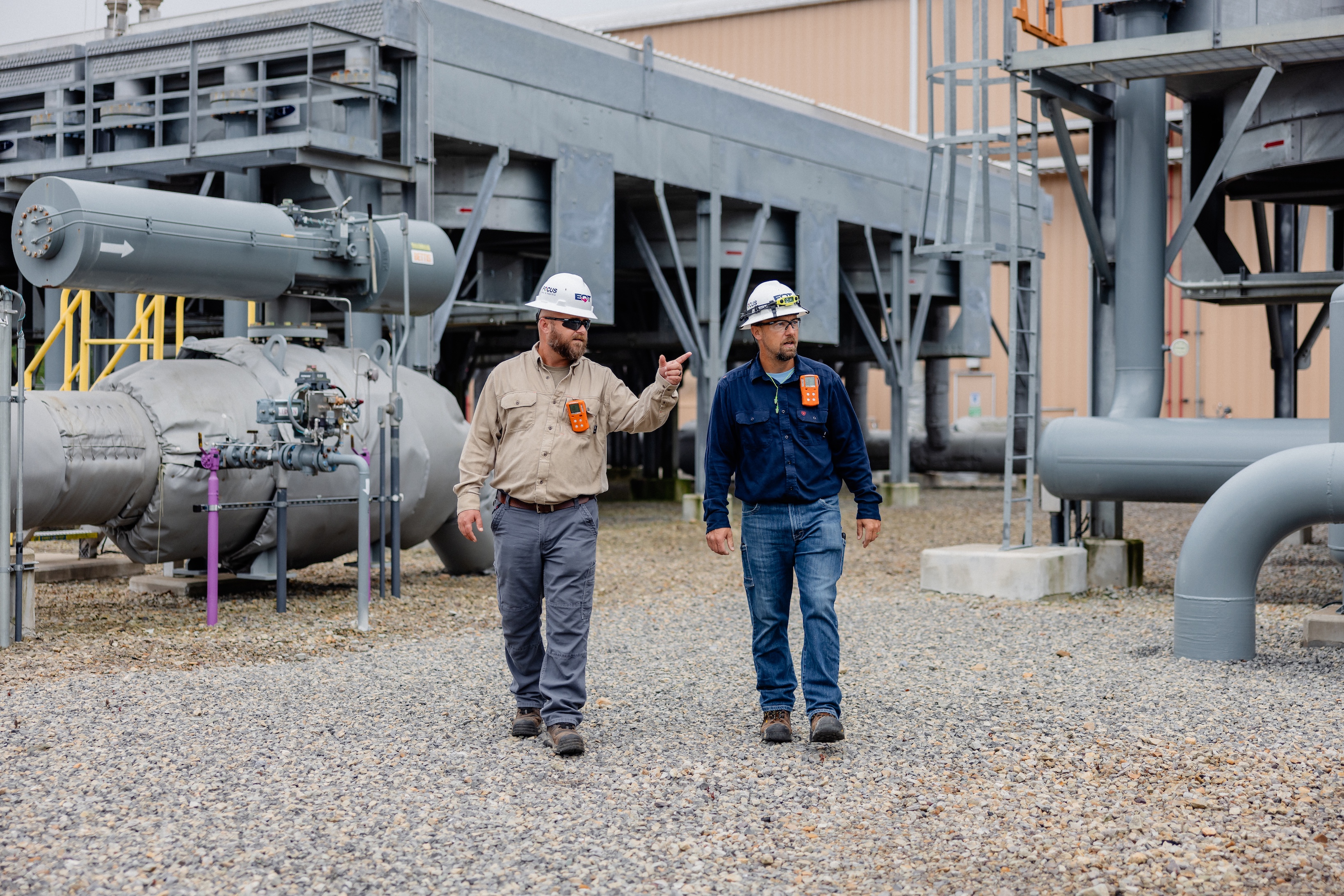 Two men in hard hats pointing at pipelines on site