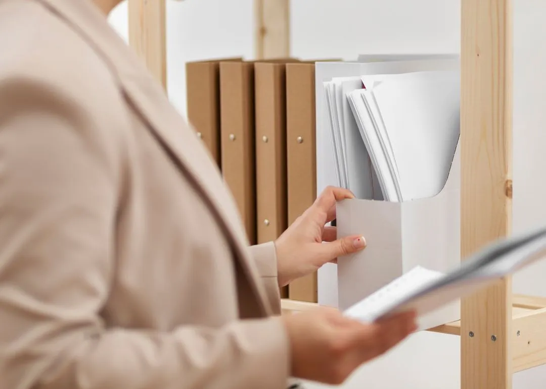 Person organizing documents on a shelf in an office