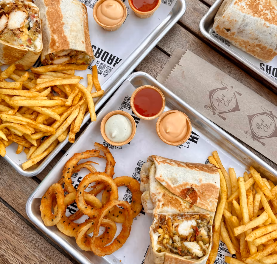 A spread of trays with burritos and fries and sauce