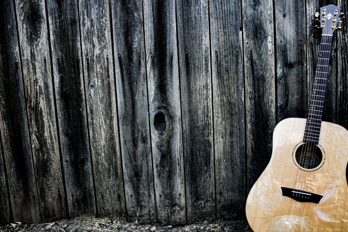 An acoustic guitar against a textured wooden wall.