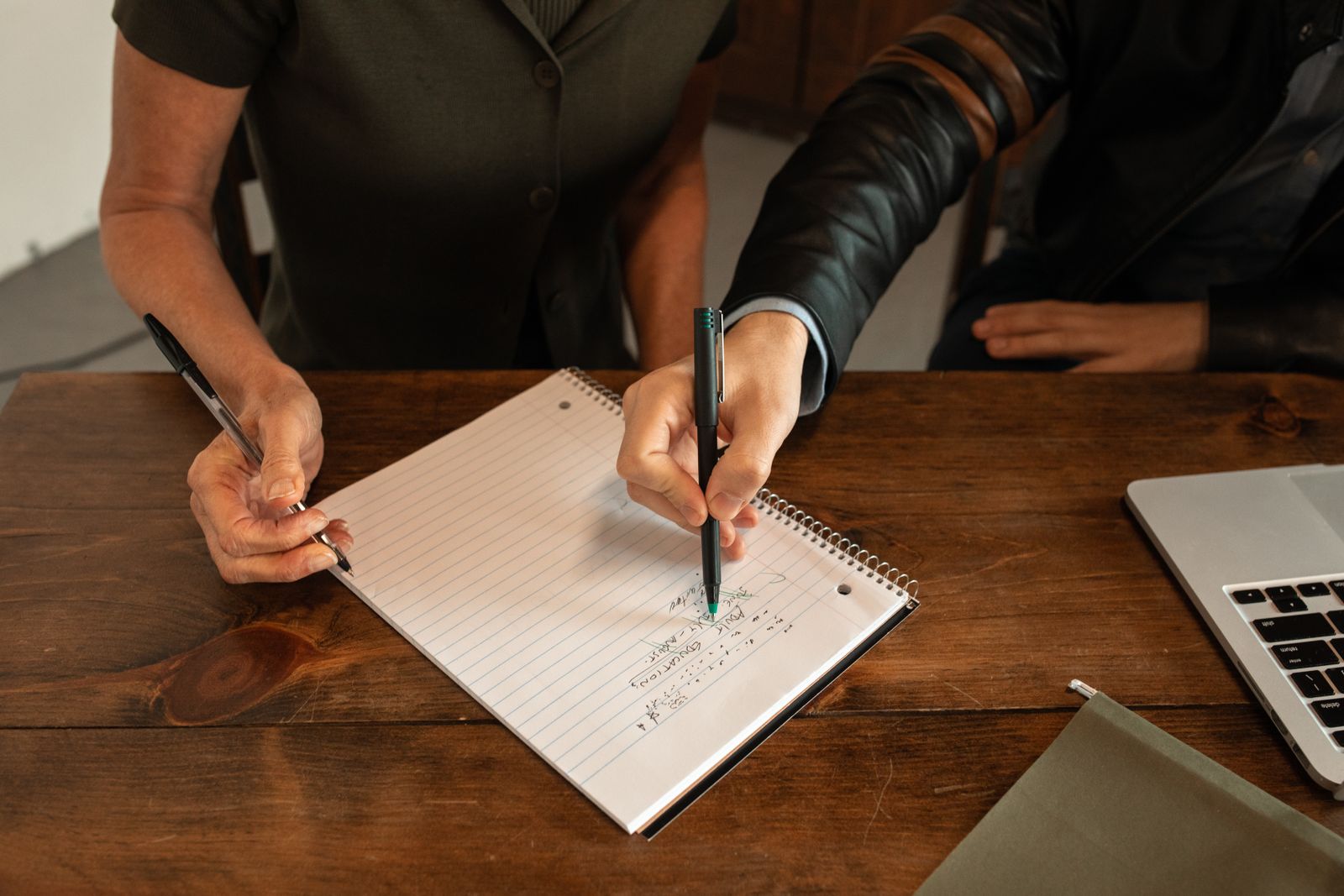 Hands taking notes with pens on a wooden table.