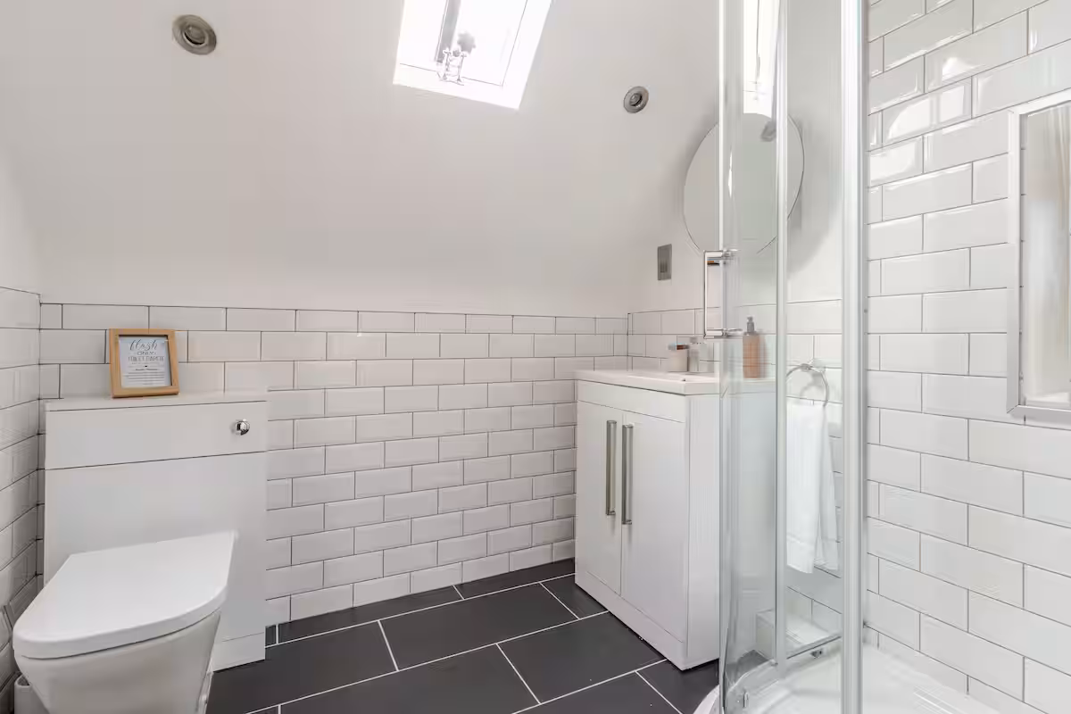 Modern bathroom with white subway tiles, black floor tiles, a toilet, a white vanity with a sink, and a glass-enclosed shower under a skylight.