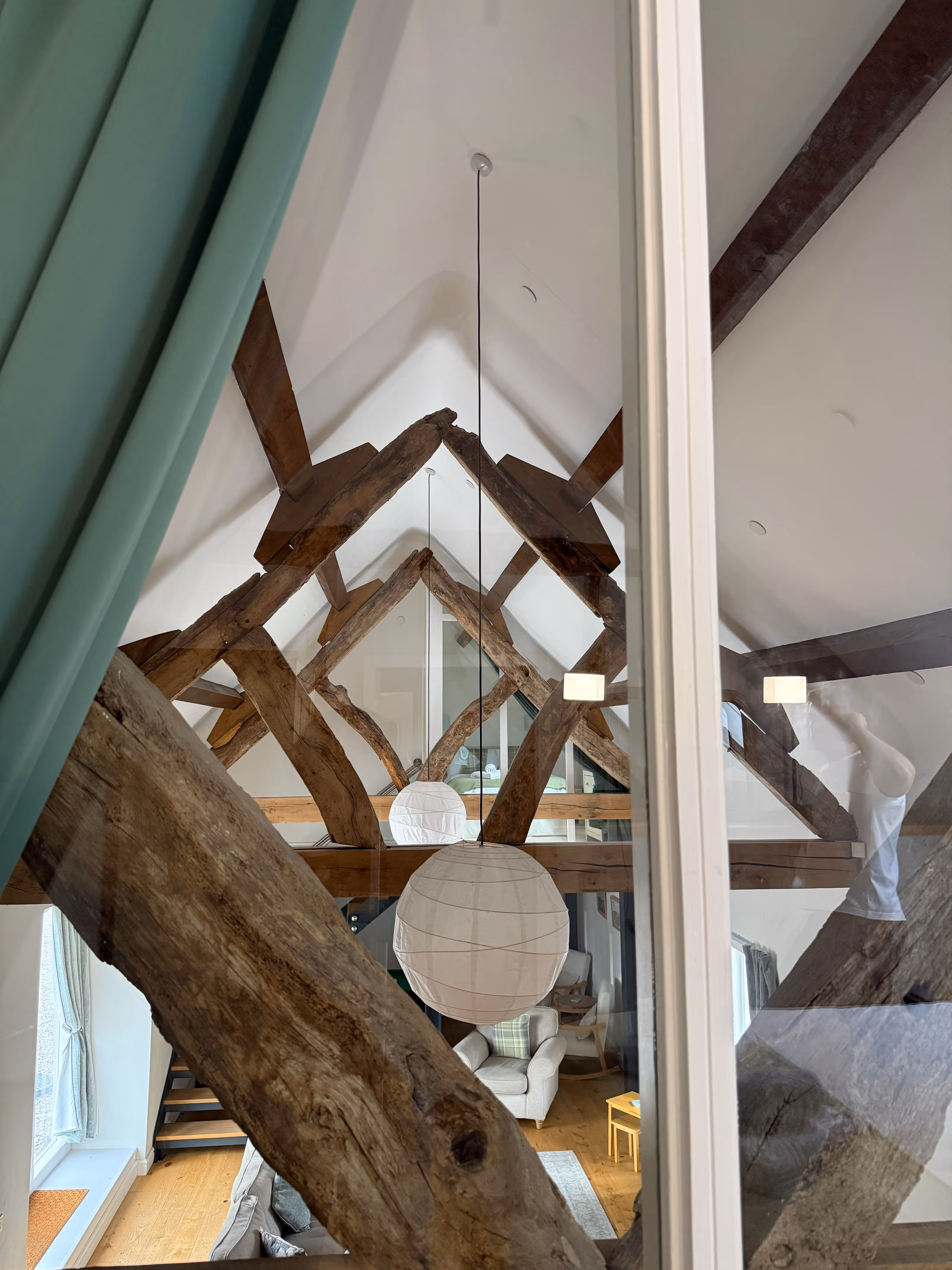 Interior view of a modern attic living space with exposed wooden beams, a white paper lantern hanging from the ceiling, and cozy furniture below.