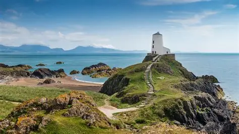 White lighthouse on a rocky, grassy promontory surrounded by sea under a partly cloudy sky.