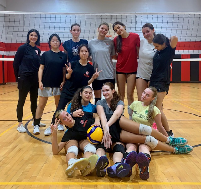 FEIA girls volleyball team and coaches pose together on the gym floor