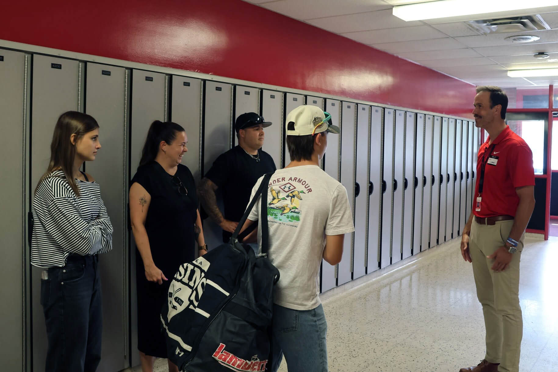FEIA staff member in a red shirt greets students and parents beside rows of lockers on a campus tour