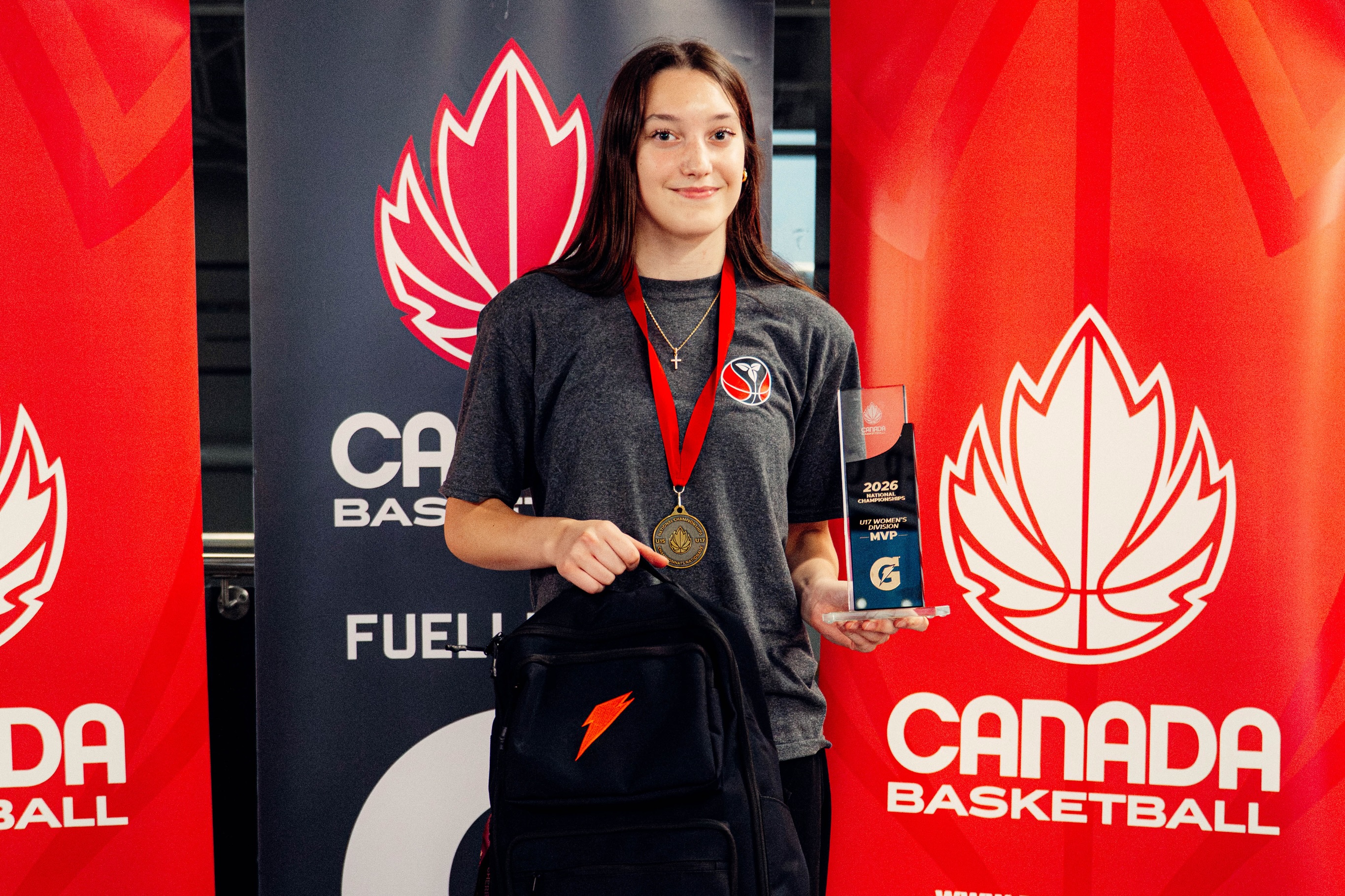 FEIA player holding a Canada Basketball medal and trophy in front of Canada Basketball banners