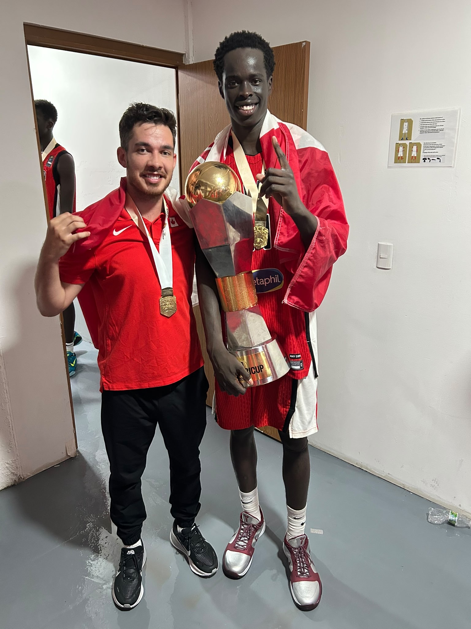 Deng Ngor with coach Steve Houston in red Team Canada gear, holding a medal and a trophy