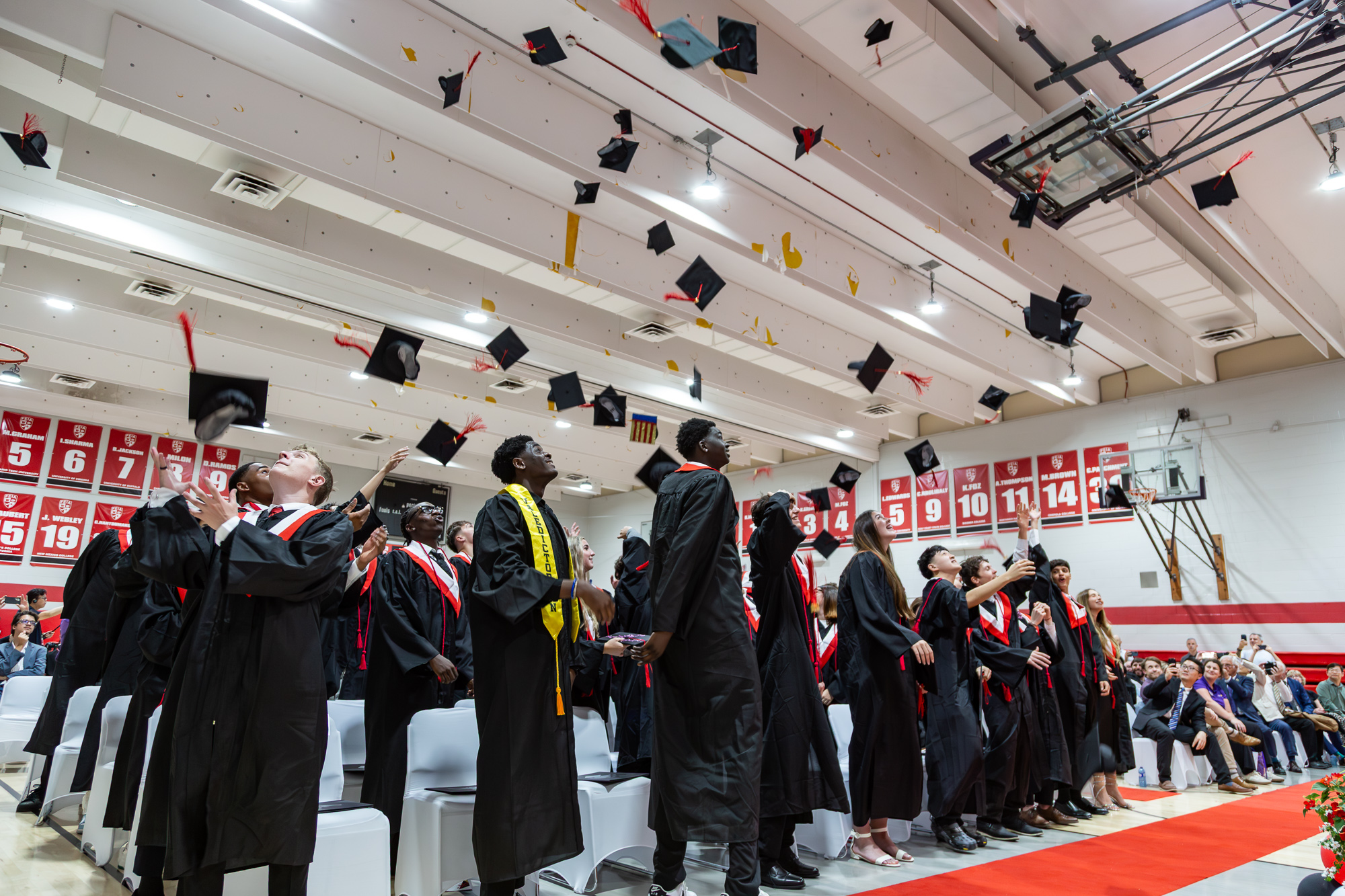 Graduates in gowns toss their caps into the air in the FEIA gym at the Class of 2026 ceremony