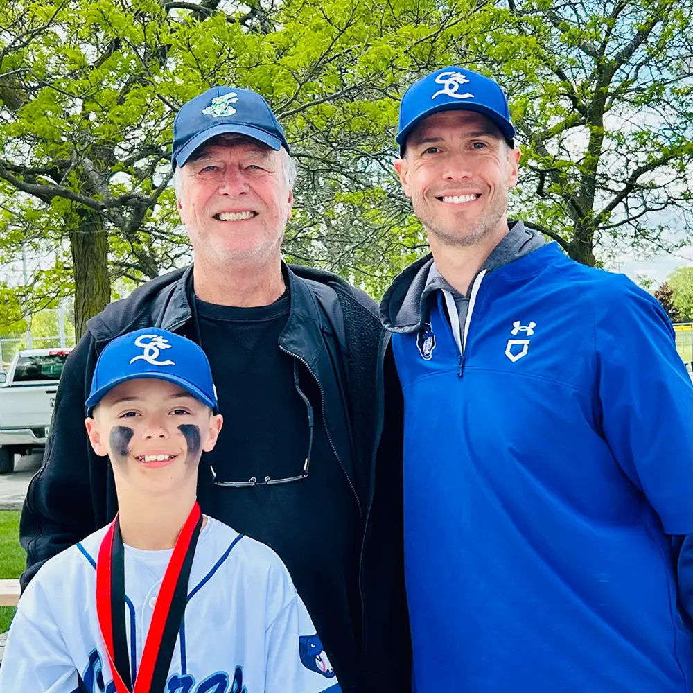 FEIA principal Mr. Cockburn with two family members, all in matching blue baseball caps outdoors