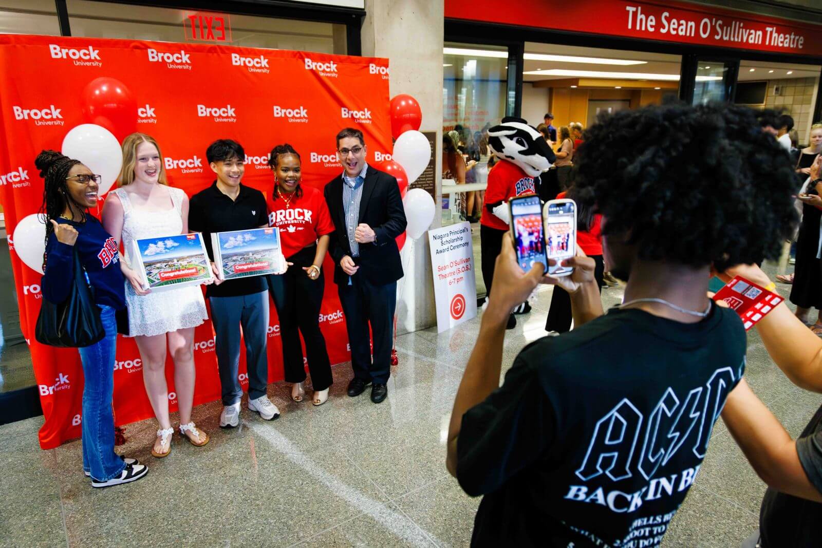 Students and staff posing with framed certificates in front of a Brock University banner at a scholarship ceremony