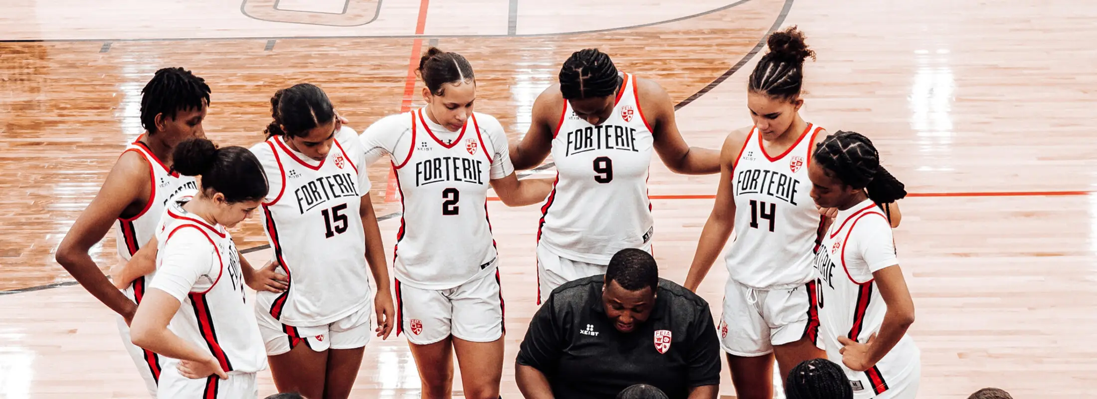 FEIA girls basketball players huddled together on the court with their coach