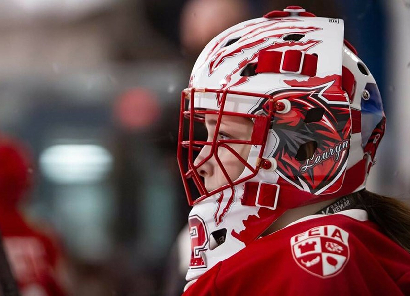 FEIA goaltender in a red mask and jersey watching play from the bench