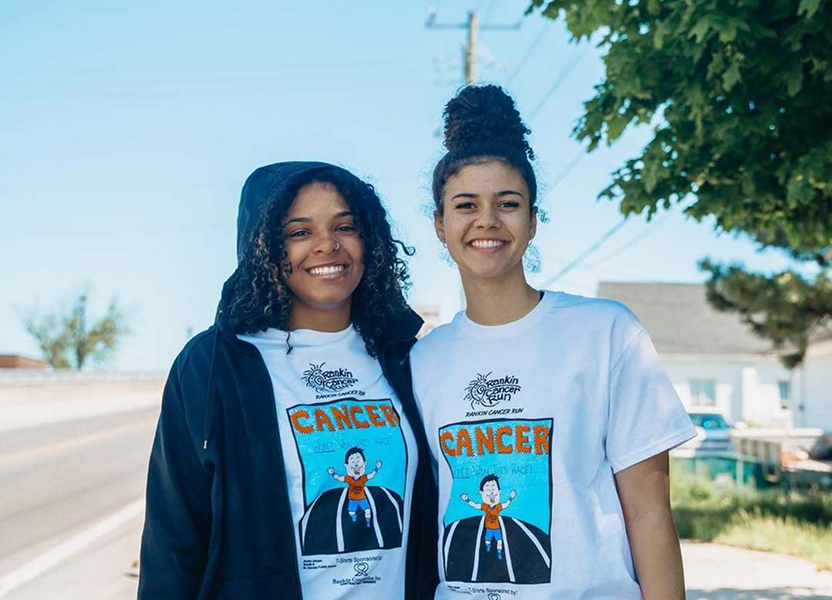 Two smiling FEIA students in matching cancer-awareness T-shirts outdoors