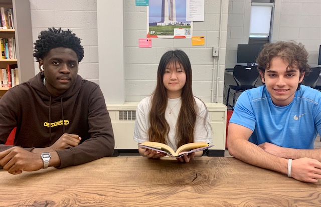 Uweoma, Victoria and Pedro, three FEIA students, seated at a table, one holding an open book