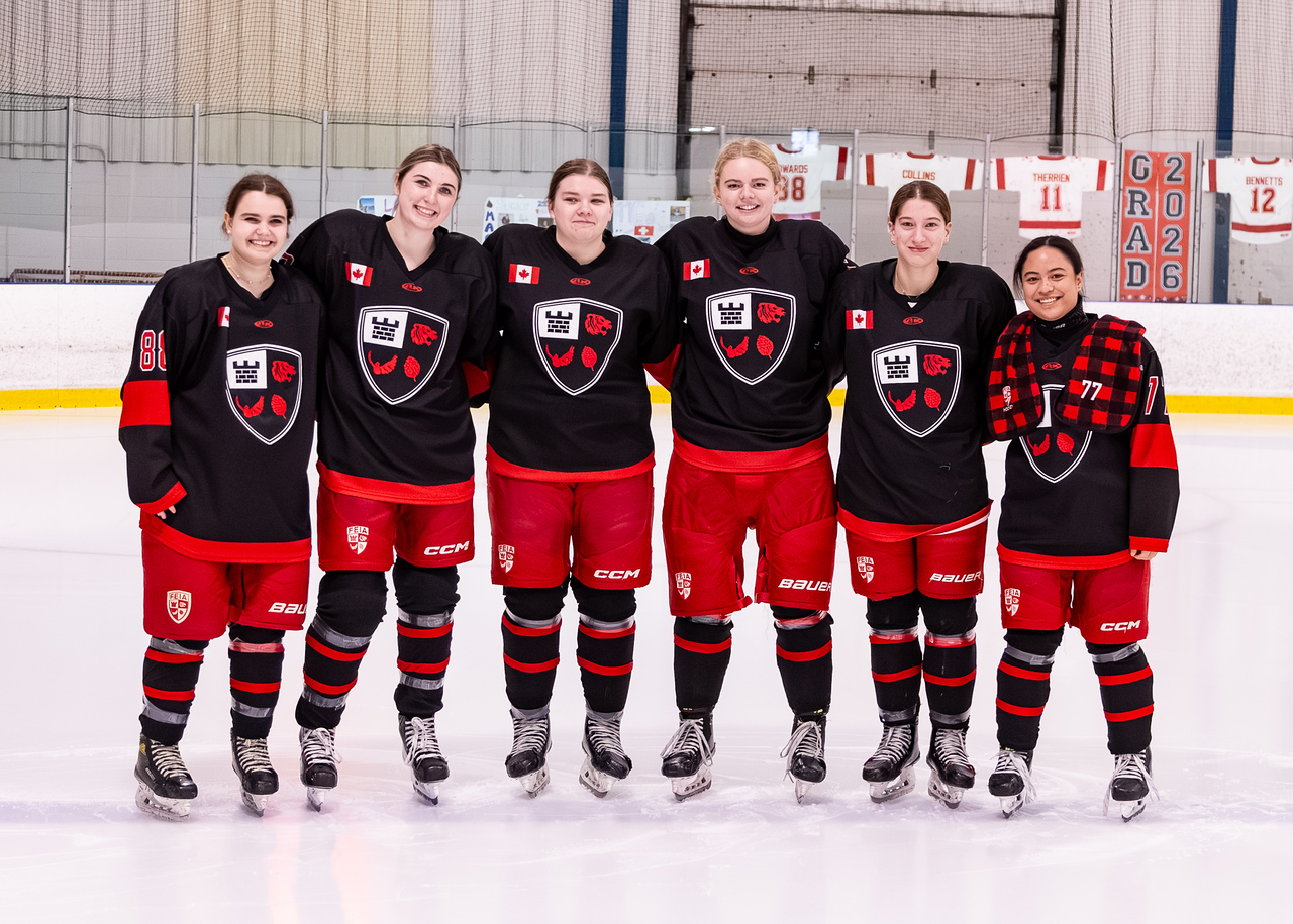Six FEIA girls hockey players in team jerseys posing together on the ice