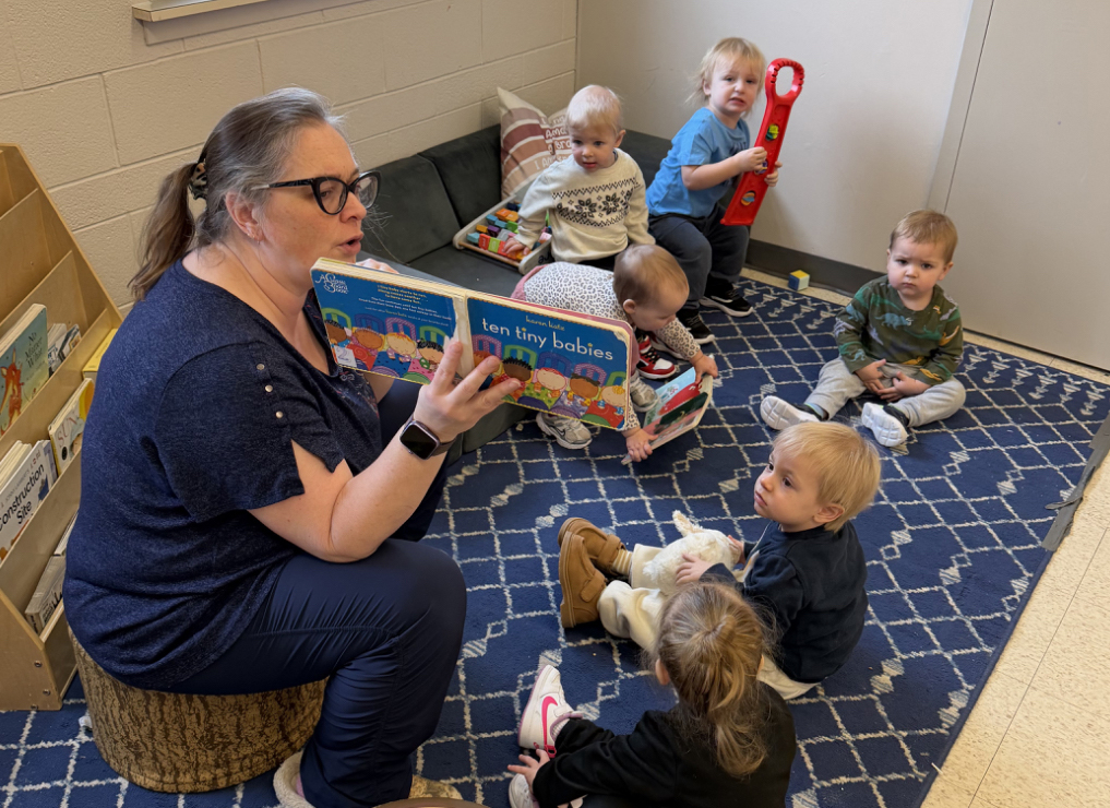 Daycare teacher reading a picture book to toddlers seated on a rug