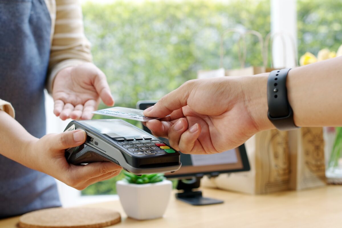 Dua tangan melakukan transaksi pembayaran menggunakan kartu di mesin EDC, melambangkan proses settlement dalam transaksi keuanga
