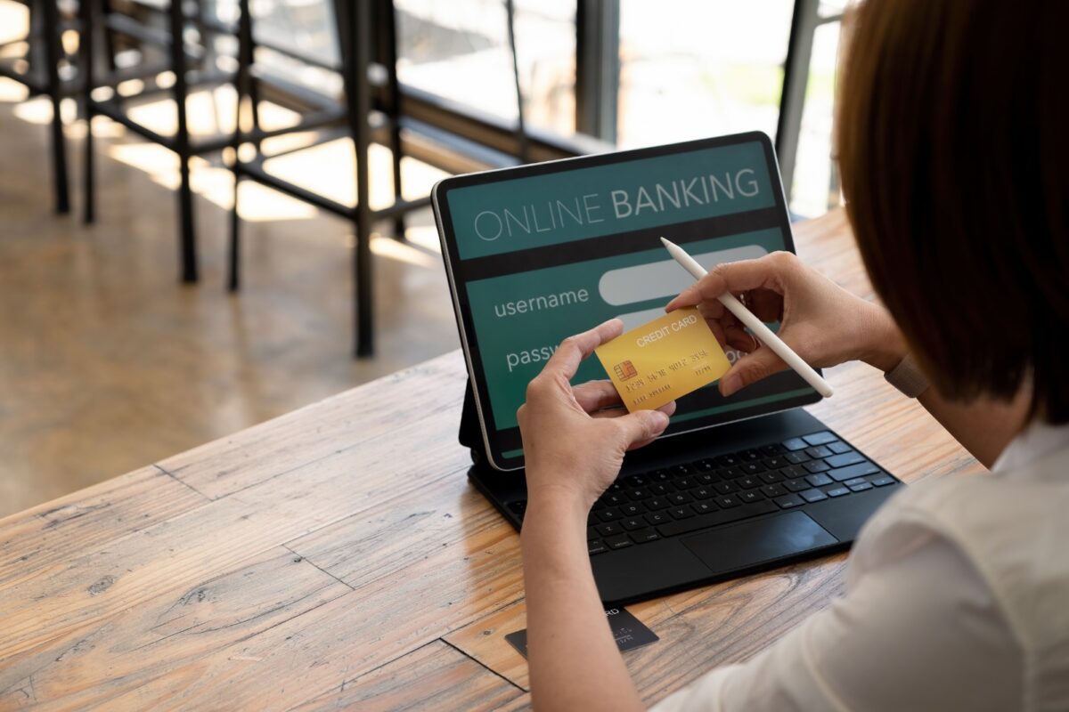 Seorang pengguna memegang kartu rekeningnya sambil bersiap melakukan transaksi online di perangkat digital, merepresentasikan proses pembayaran melalui bank transfer payment gateway, yang menghubungkan pembeli, merchant, dan bank untuk memastikan transaksi berlangsung aman dan efisien.