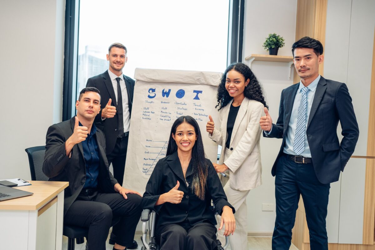 Sekelompok pegawai sedang berdiskusi di depan papan tulis penuh diagram dan catatan strategi, membahas analisis SWOT adalah metode penting untuk merancang rencana bisnis yang efektif