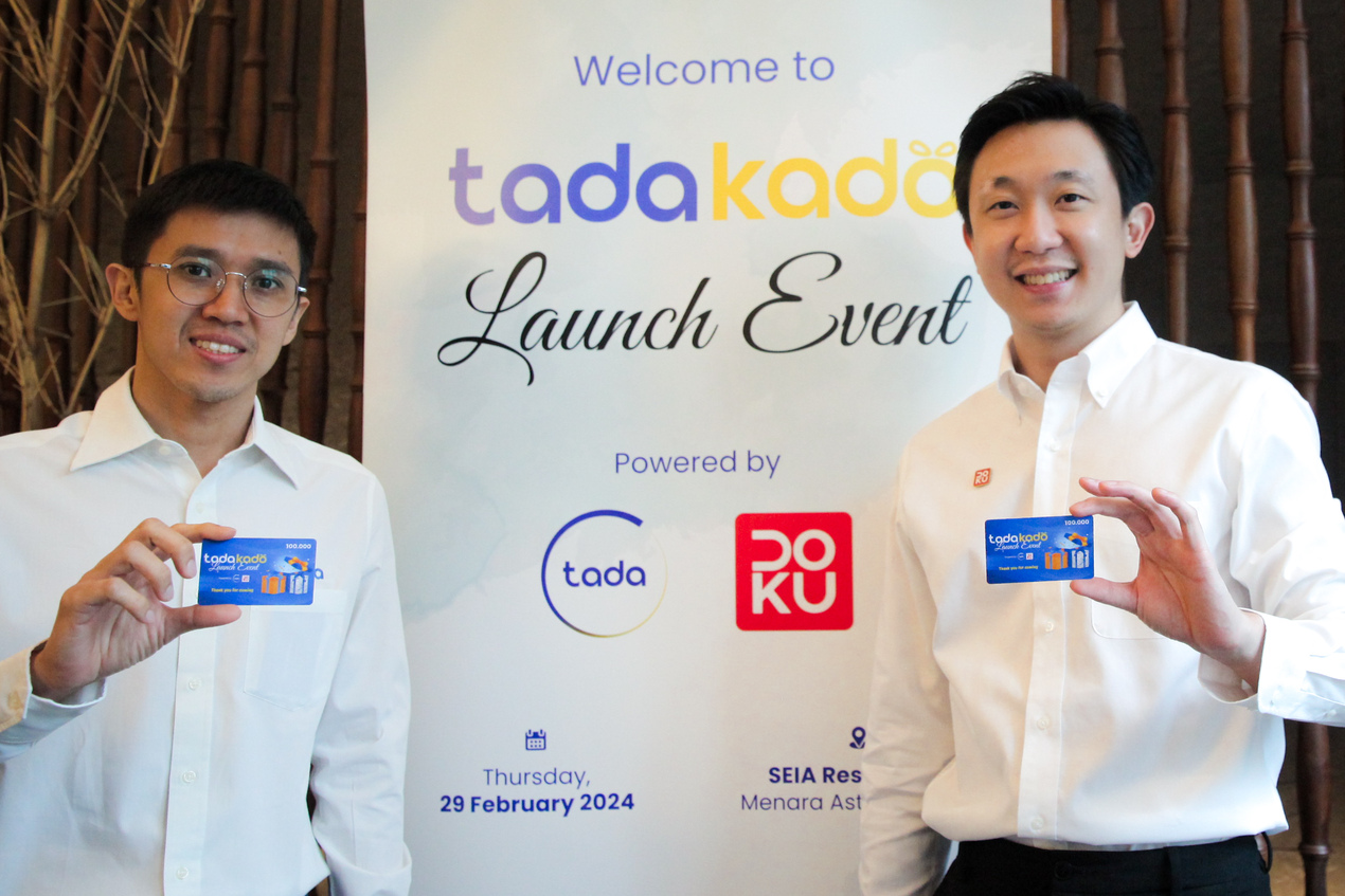 Dua pria berfoto sambil memegang kartu Tadakado saat acara peluncuran Tadakado yang didukung oleh DOKU dan Tada, dengan backdrop bertuliskan “Tadakado Launch Event” pada 29 Februari 2024.