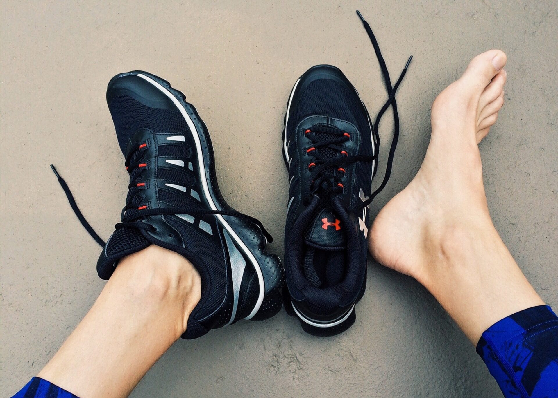 Showcasing the importance of foot care with a person's feet in running shoes on a concrete floor.