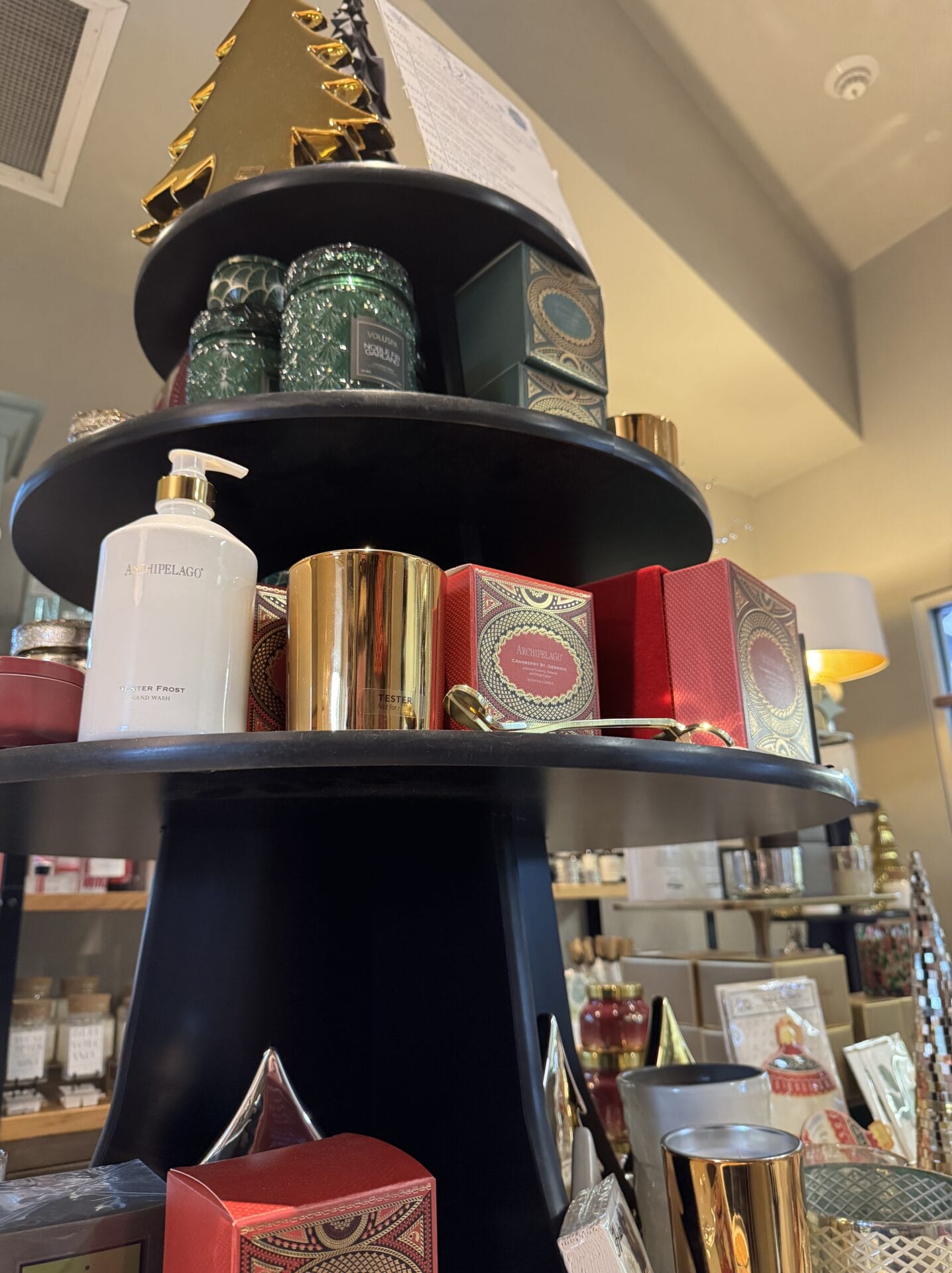 A display shelf brimming with holiday-themed products, including candles, boxed items, and decorative pieces, captures the festive spirit of Christmas shopping in a store setting.