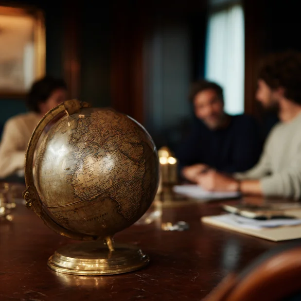 Vintage globe on a wooden table with three people blurred in the background having a discussion.