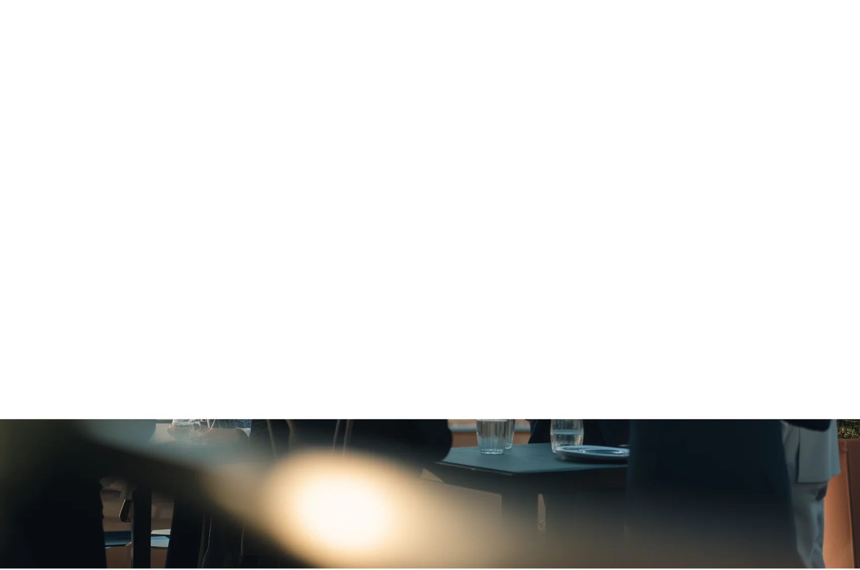 Blurred foreground light with people sitting at a table with glasses and plates in the background.