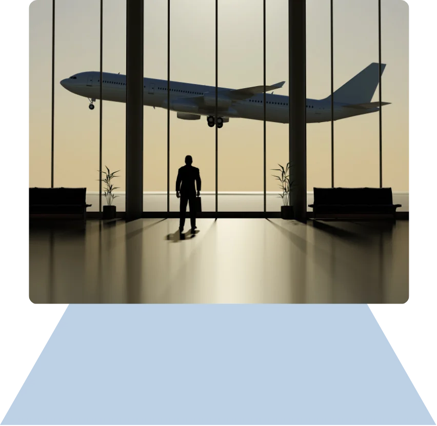 Silhouette of a man with a briefcase standing in an airport terminal watching an airplane take off through large windows at sunset.