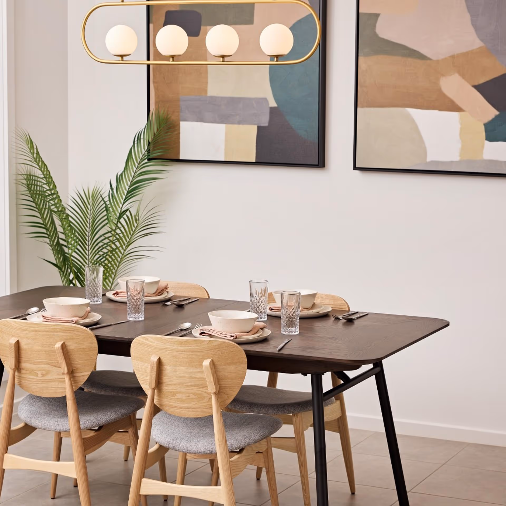 Modern dining room featuring a dark wood table with four light wooden chairs, abstract art, and a gold light fixture; a calm, elegant setting.
