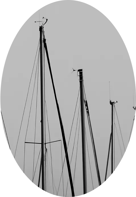 Black and white photo of several sailboat masts set against a plain, light sky, framed in an oval shape.