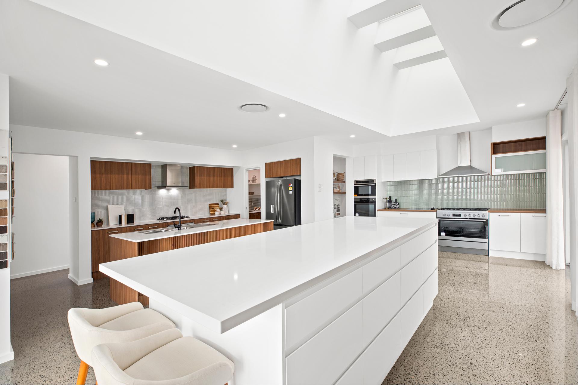 Modern kitchen with white cabinetry, large island, and skylights. Stainless steel appliances and wood accents add warmth. Sleek, minimalist design.