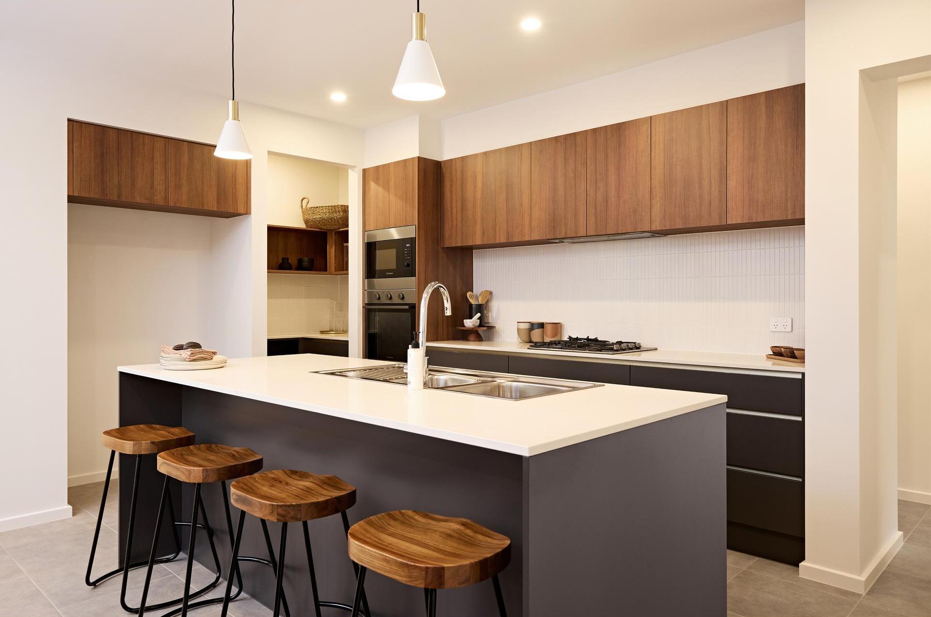 Modern kitchen with wooden cabinets, large island with white countertop and sink, four wooden stools, pendant lights, and modern appliances.