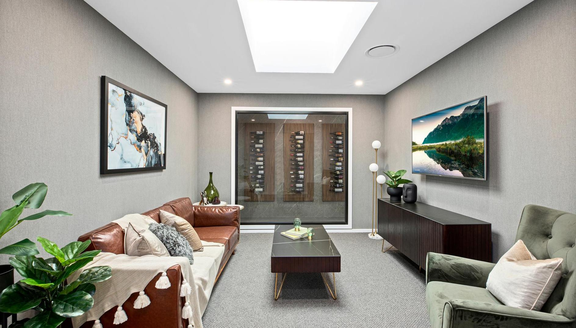 A modern, cozy living room with a skylight. Features a brown leather sofa, green armchair, art, TV, and built-in wine display. Neutral tones and plants add warmth.