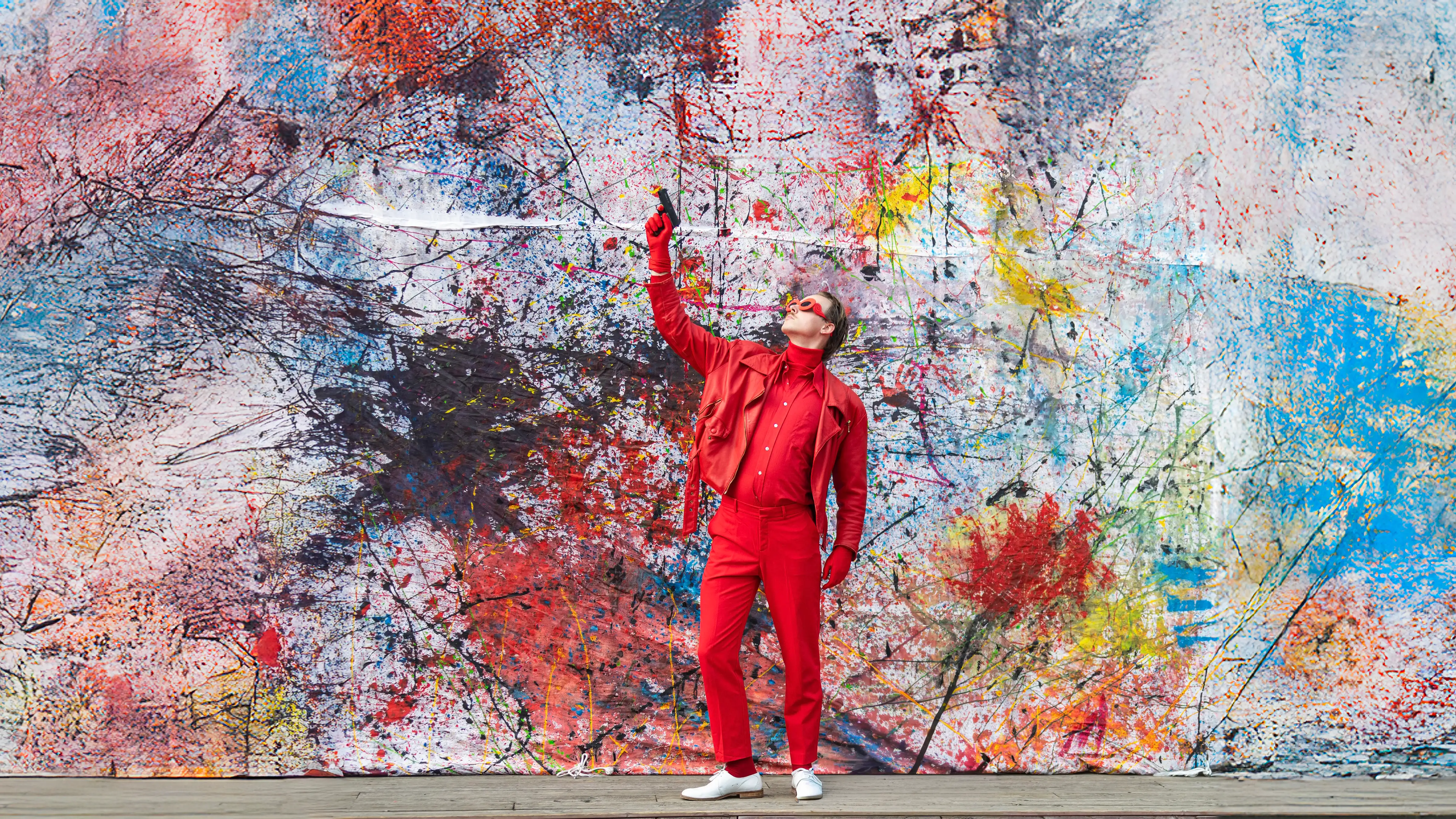 Man met zonnebril voor een schilderdoek richt een alarmpistool naar de hemel