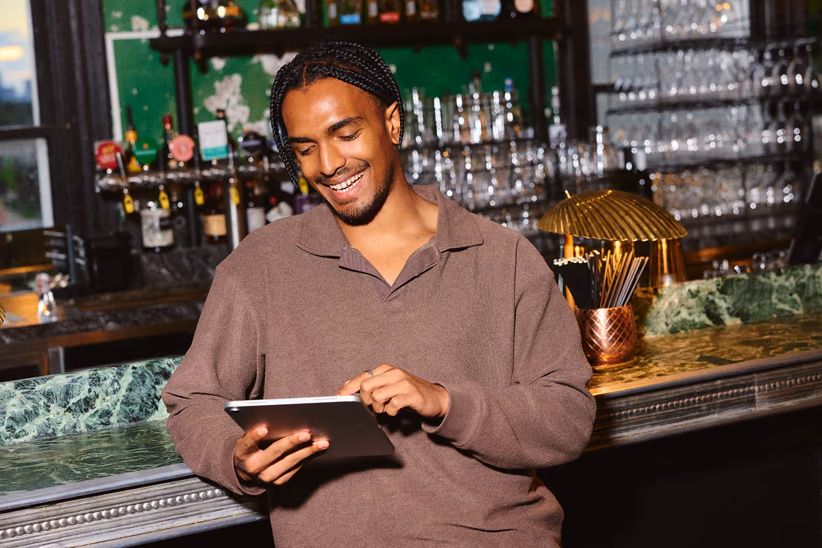 A man leaning on the bar using the me&u reservation platform on iPad