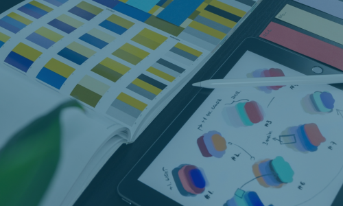 Tablet displaying color swatches and a stylus pen, beside an open color palette book and sample cards.