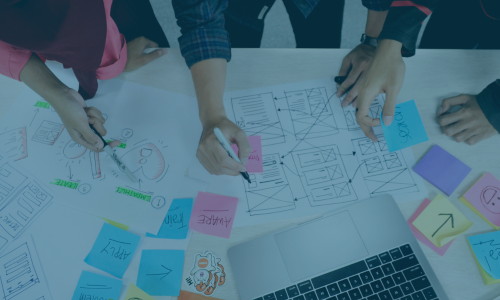 Overhead view of people collaborating on website wireframes with sticky notes and a laptop on a table.