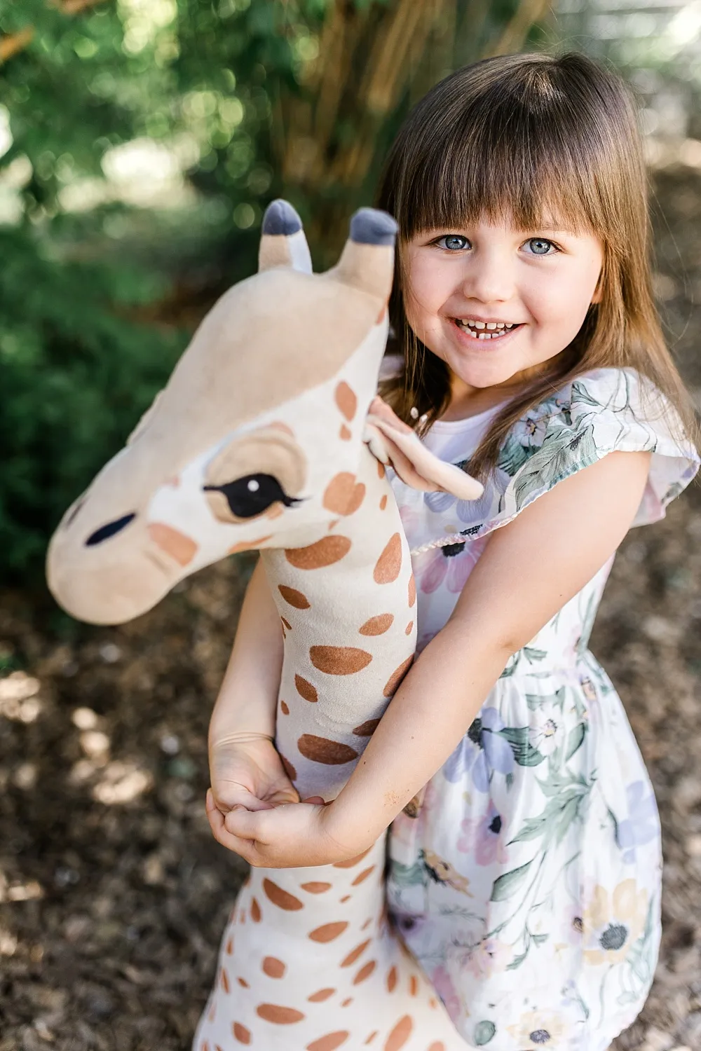 Lächendes Mädchen umarmt ein großes Plüschgiraffen-Spielzeug im Freien.
