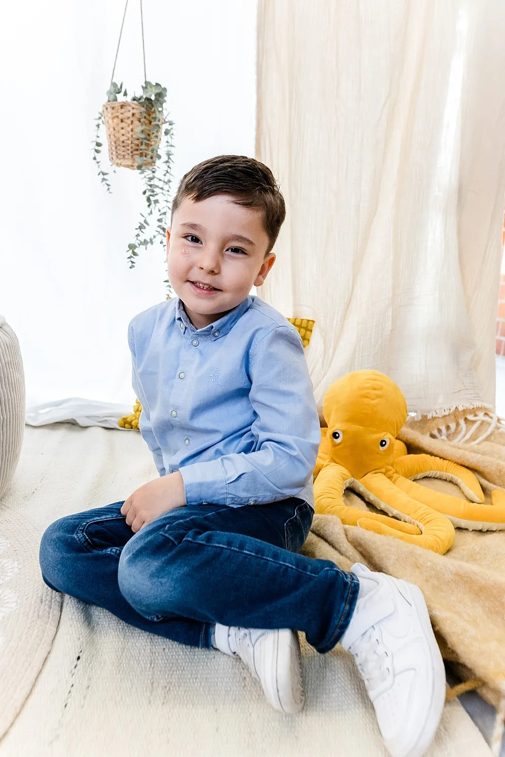 Lächelnder Junge sitzt gekreuzt auf dem Boden neben einem großen gelben Plüsch-Oktopus.