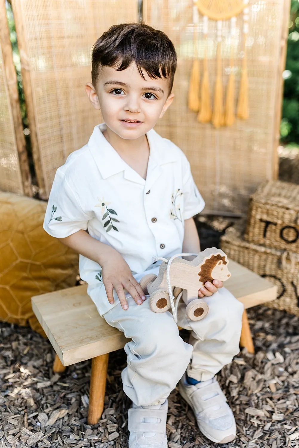 Kleiner Junge sitzt auf einer Holzbank und hält ein hölzernes Löwen-Spielzeug mit Rädern.