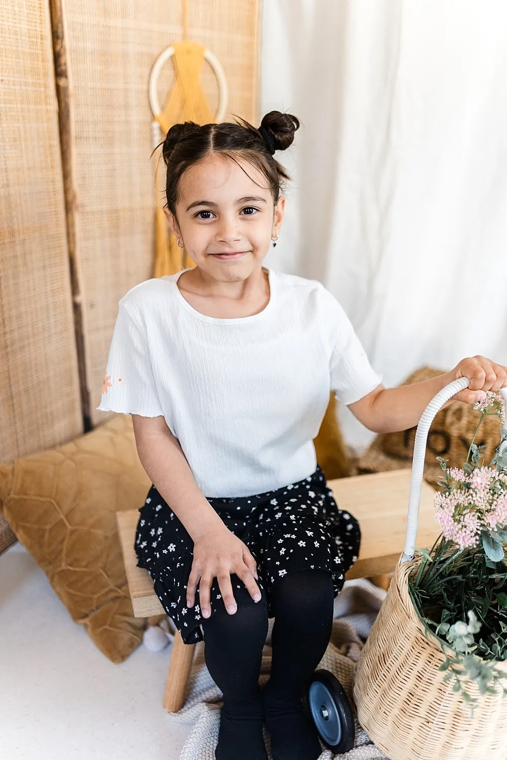 Mädchen mit weißen T-Shirt und schwarzem Rock sitzt auf einer Bank und hält einen Korb mit Blumen.
