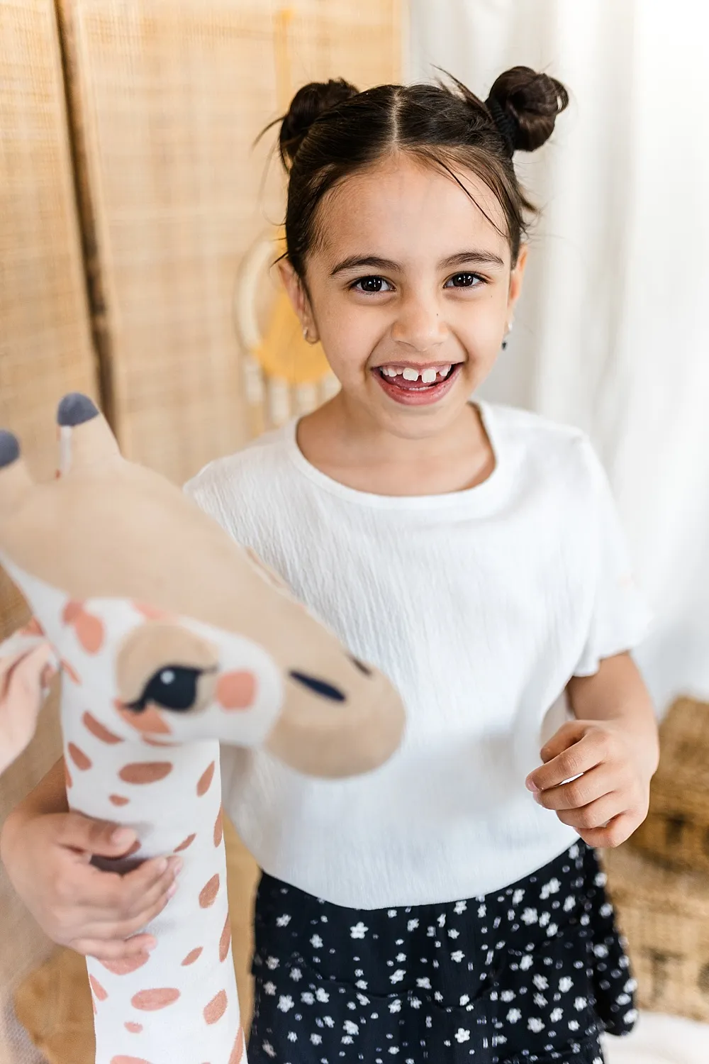 Fröhliches Mädchen mit zwei Haarknoten hält ein Plüschgiraffen-Spielzeug.
