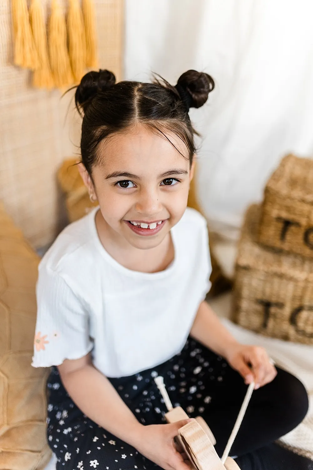 Fröhliches Mädchen mit zwei Duttfrisuren, das ein Holzspielzeug in den Händen hält.