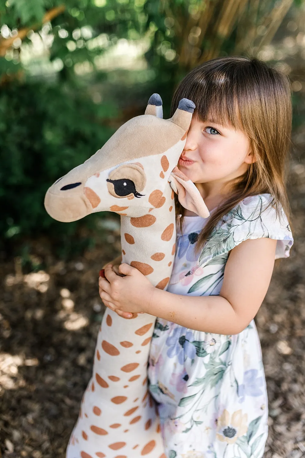Ein kleines Mädchen umarmt eine große Plüschgiraffe im Freien.