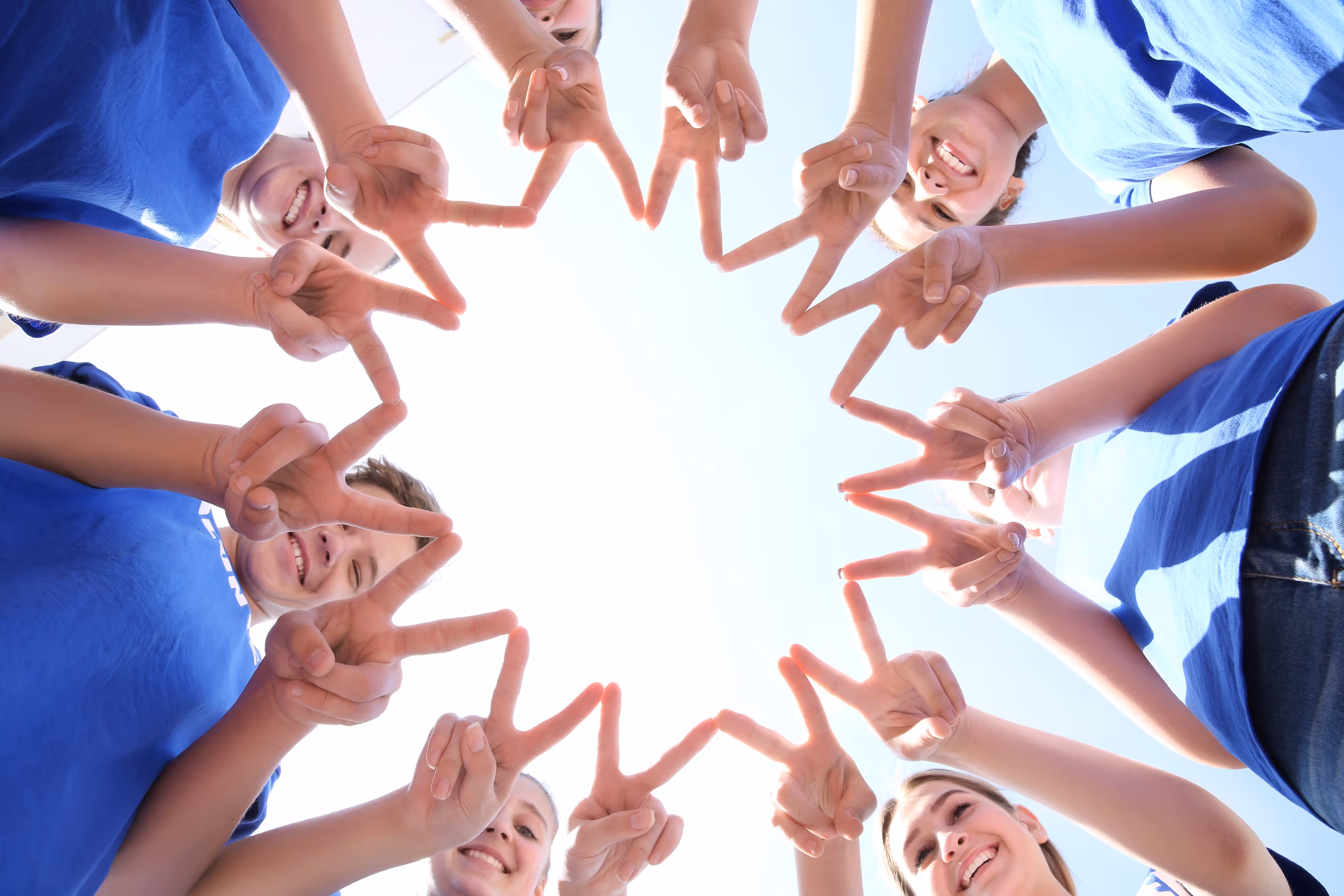 Teammitglider stehen im Kreis zusammen, zeigen jeweils mit beiden Händen das Victory-Zeichen und bilden dadurch gemeinsam einen Stern.