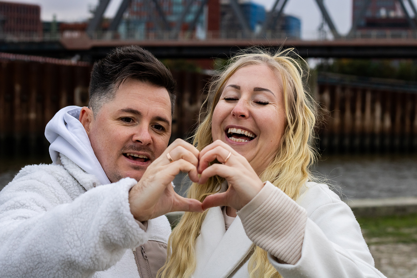 Ein Paar formt aus Händen ein Herz und lacht dabei.