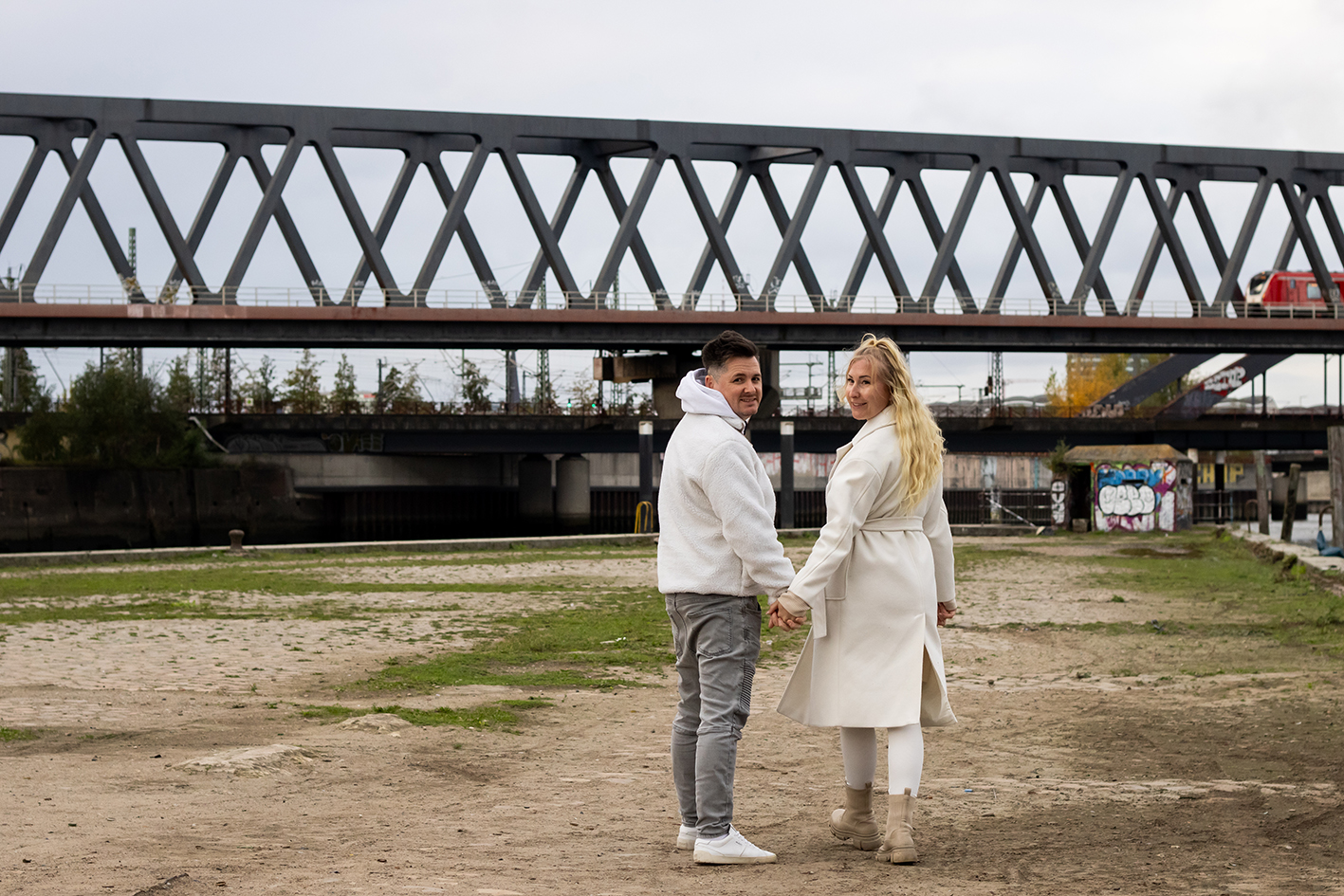 Ein Paar läuft Händchen haltend spazieren. Sie schauen über die Schulter Richtung Kamera.