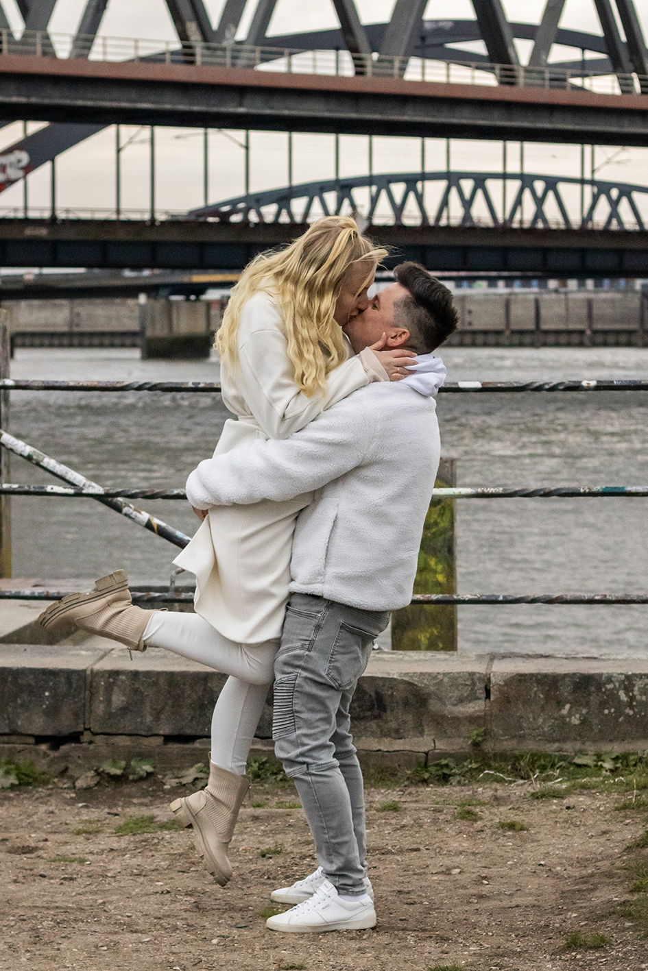 Ein Paar küsst sich. Er hebt sie hoch. Im Hintergrund Brücken und Wasser.